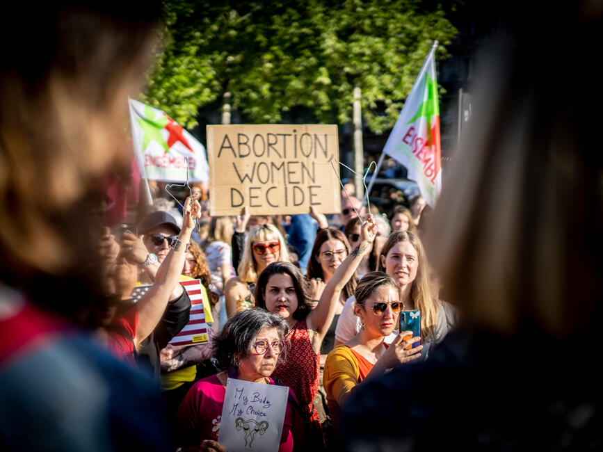 Eine Menschenmenge bei einer Kundgebung bei sonnigem Wetter. Auf einem Schild steht "Abortion Women Decide". 