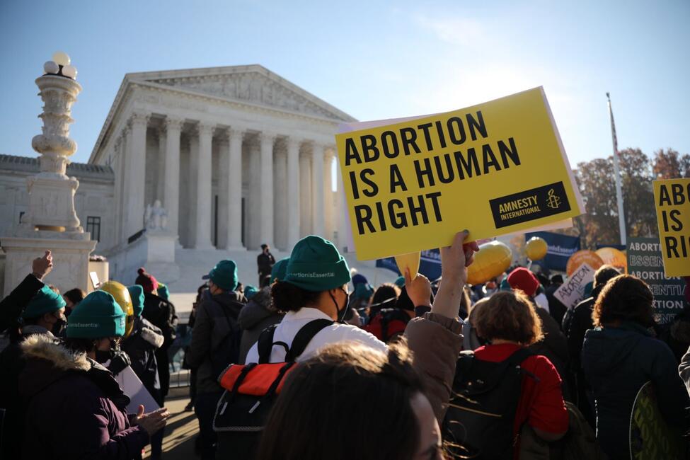 Viele Menschen von hinten bei einer Kundgebung vor dem Supreme-Court-Gebäude in Washington D.C., auf einem großen gelben Amnesty-Schild steht "Abortion is a human right". 