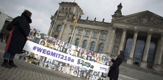Zwei Frauen stehen vor dem Reichstagsgebäude in Berlin und halten ein großes Plakat hoch auf dem steht "Weg mit 219a" 