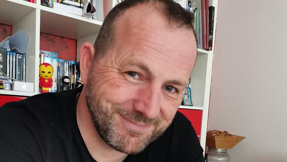 Der Gewerkschafter Frédéric Vuillaume lächelt an einem Tisch in die Kamera, 21. April 2021