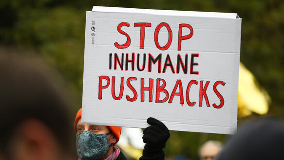 Das Bild zeigt eine Perspn, die ein Schild hält "Stop inhumane Pushbacks"