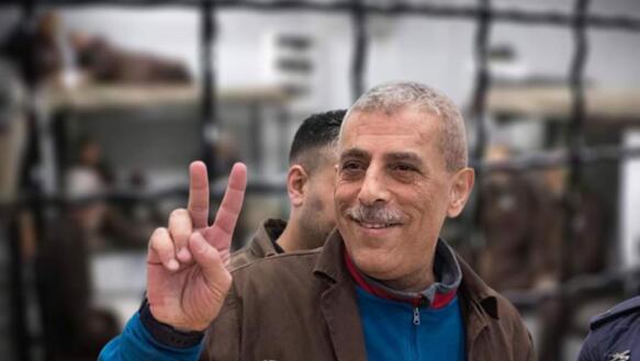 Ein älterer Mann mit kurzen grauen Haaren lächelt und formt mit Zeige- und Mittelfinger ein "V", es ist Walid Daqqah. 