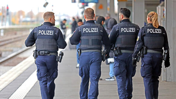 Das Bild zeigt vier Personen in Polizei-Uniformen von hinten fotografiert auf einem Bahnsteig-