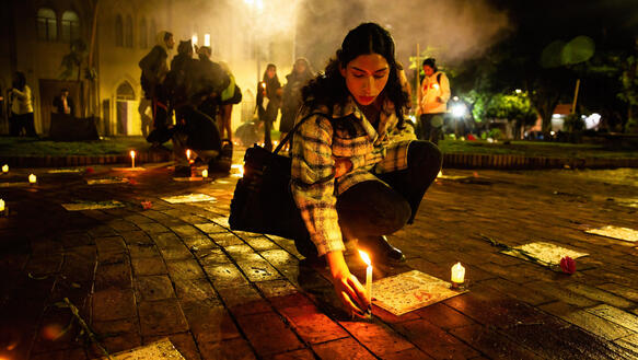 Das Bild zeigt eine Frau, die eine Kerze anzündet und sie auf den Asphalt stellt.