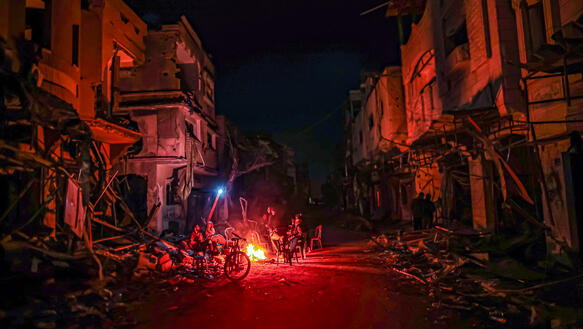 Menschen wärmen sich nachts in in der palästinensischen Stadt Chan Yunis im Gazastreifen an einem Feuer inmitten der Ruinen von Häusern, die bei israelischen Angriffen zerstört wurden (26. November 2023).