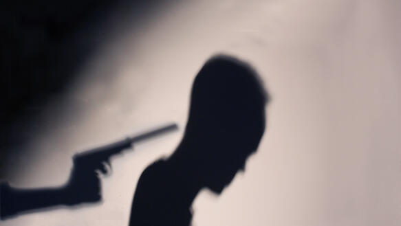 Silhouette eines Mannes, dem eine Pistole an den Hinterkopf gehalten wird