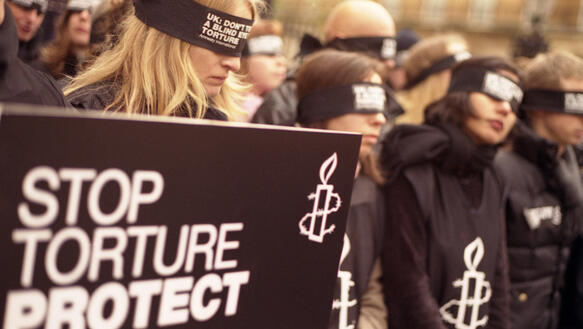 Schwarz gekleidetet Menschen protestieren mit verbundenen Augen und einem schwarzen Plakat