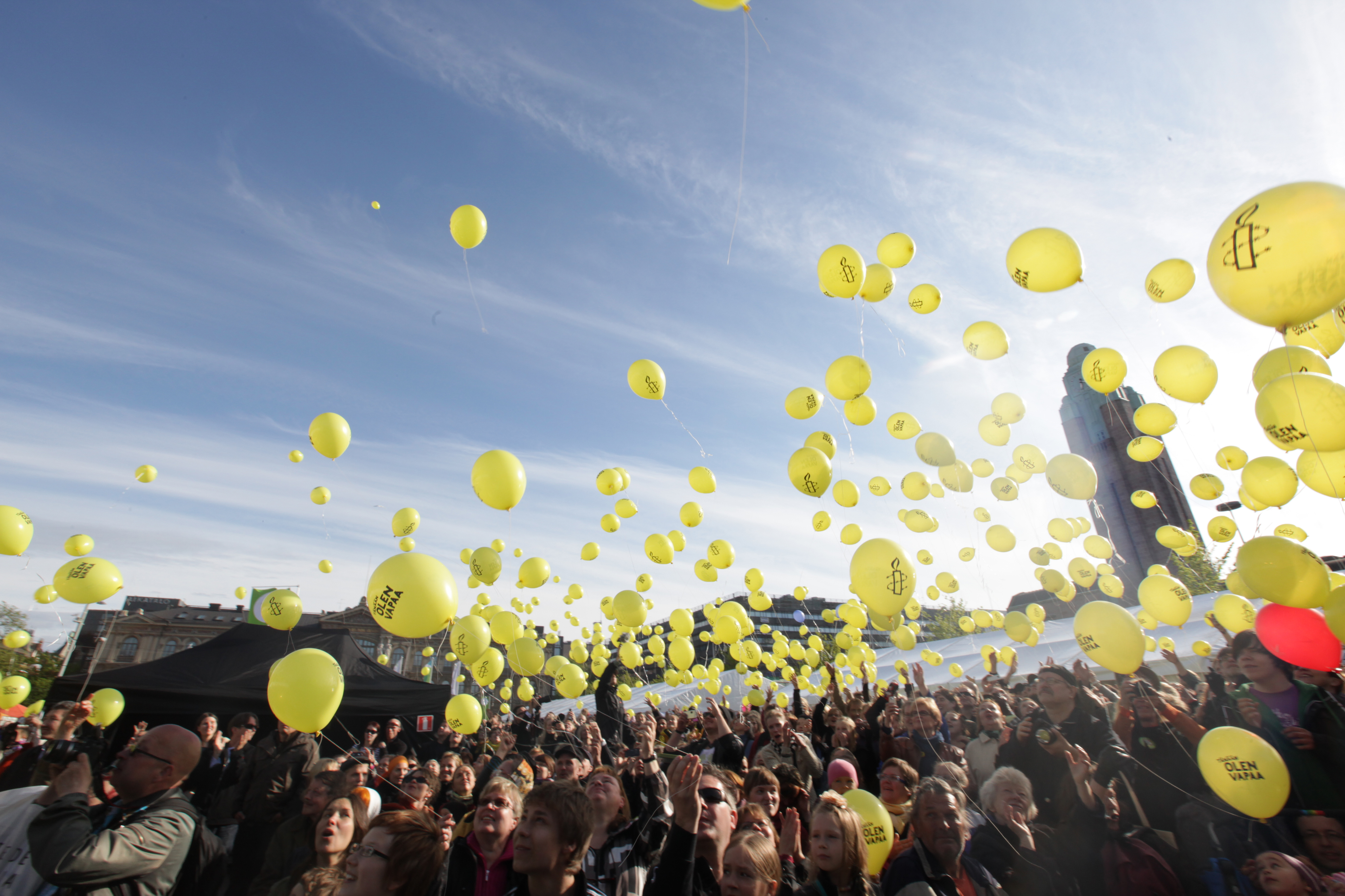Menschenmenge lässt gelbfarbene Luftballons in den Himmel steigen