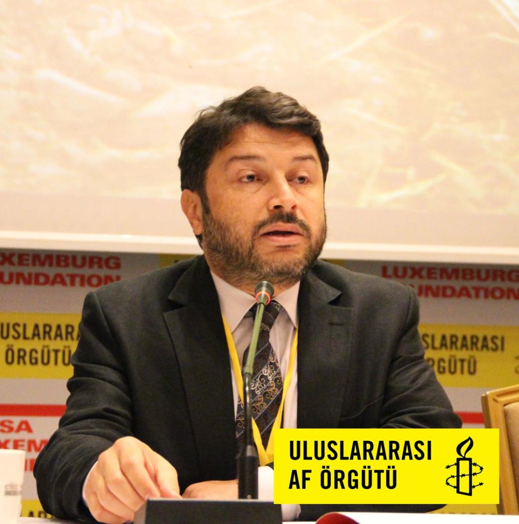 Taner Kılıç sitzt an einem Tisch, vor ihm ein Mikrofon