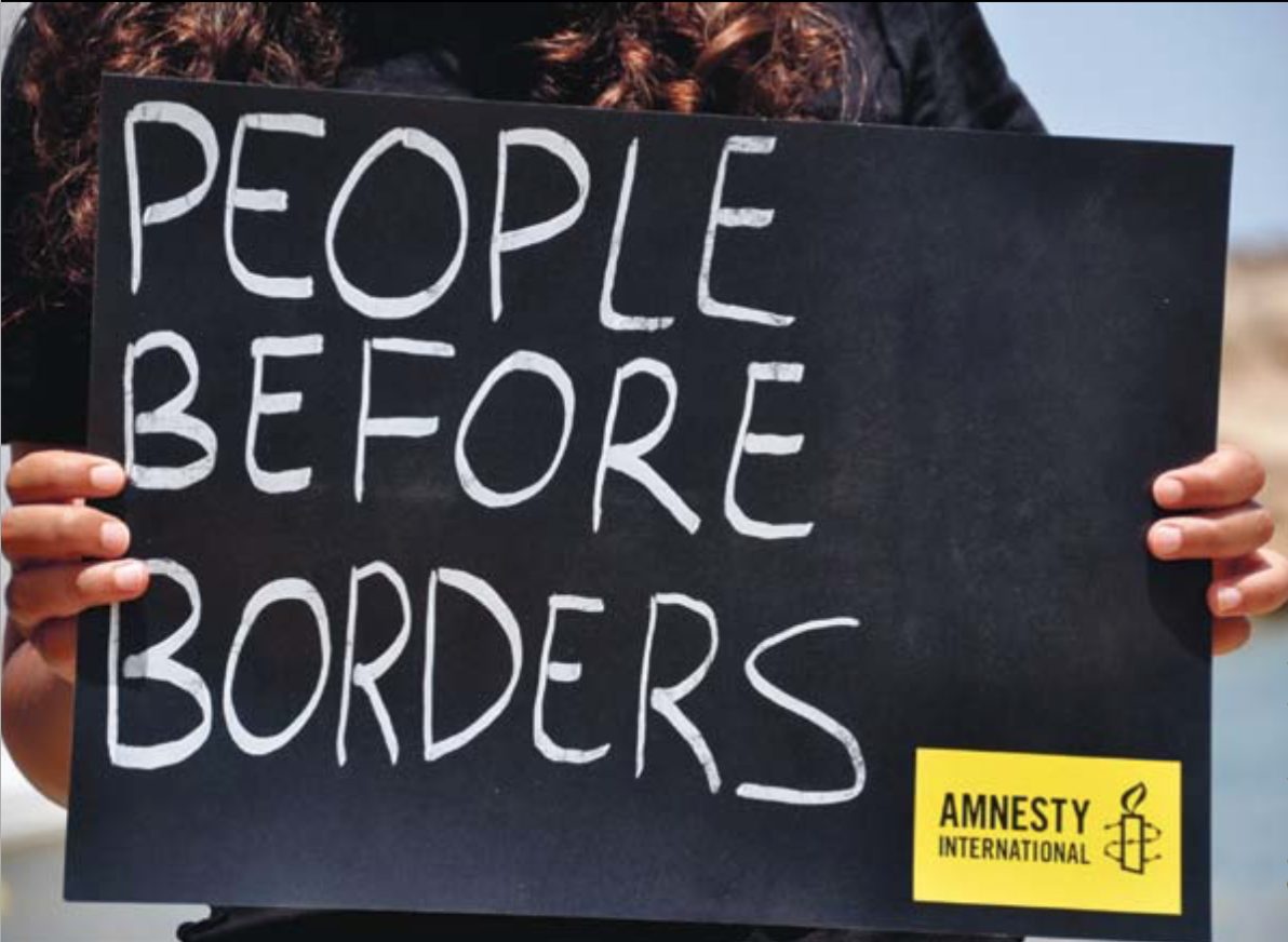Ein Schild mit der Aufschrift "People before borders" wird groß in den Bildausschnitt gehalten.