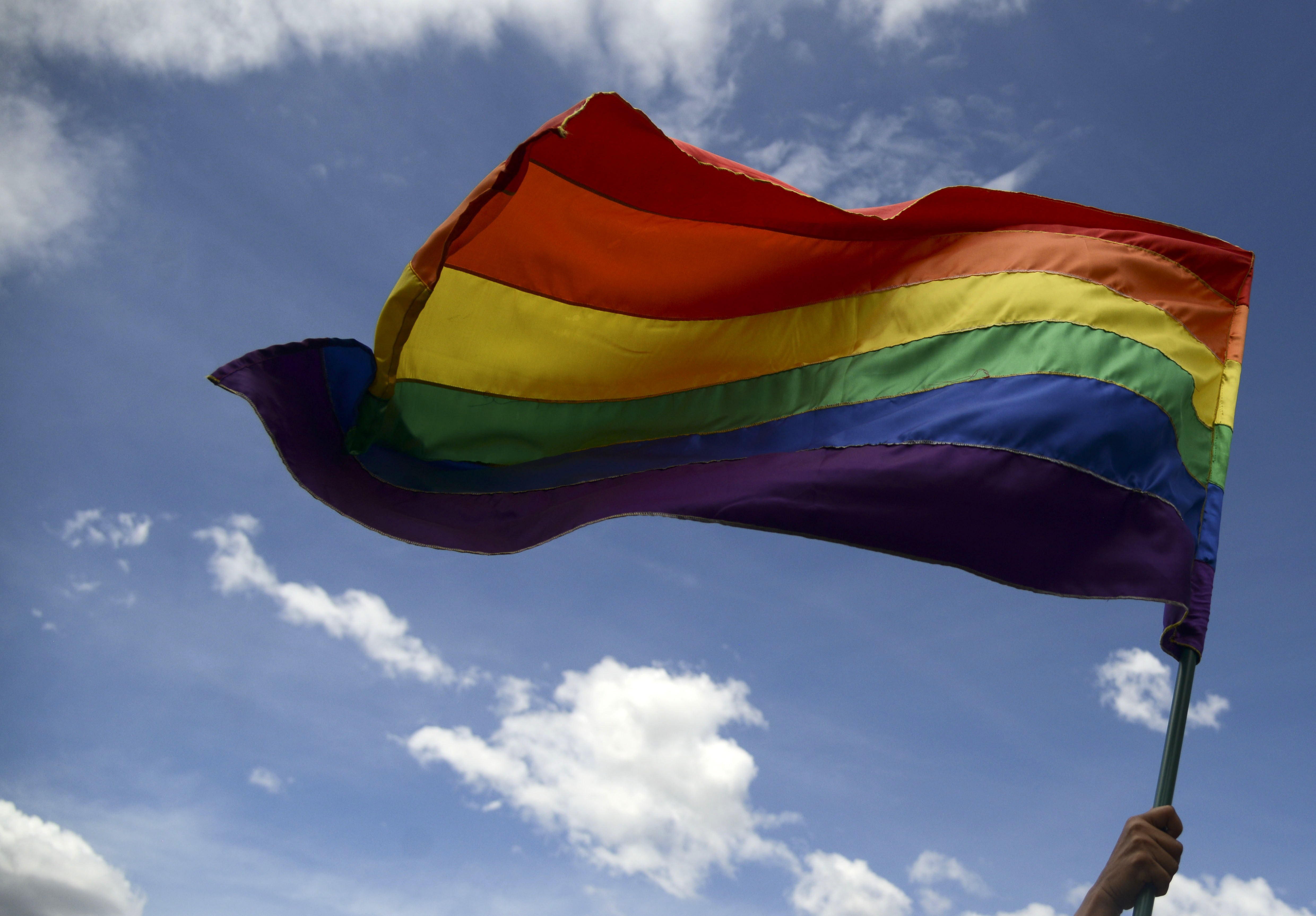 Regenbogenfahne weht in der Luft vor blauem Himmel mit wenigen kleinen Wolken