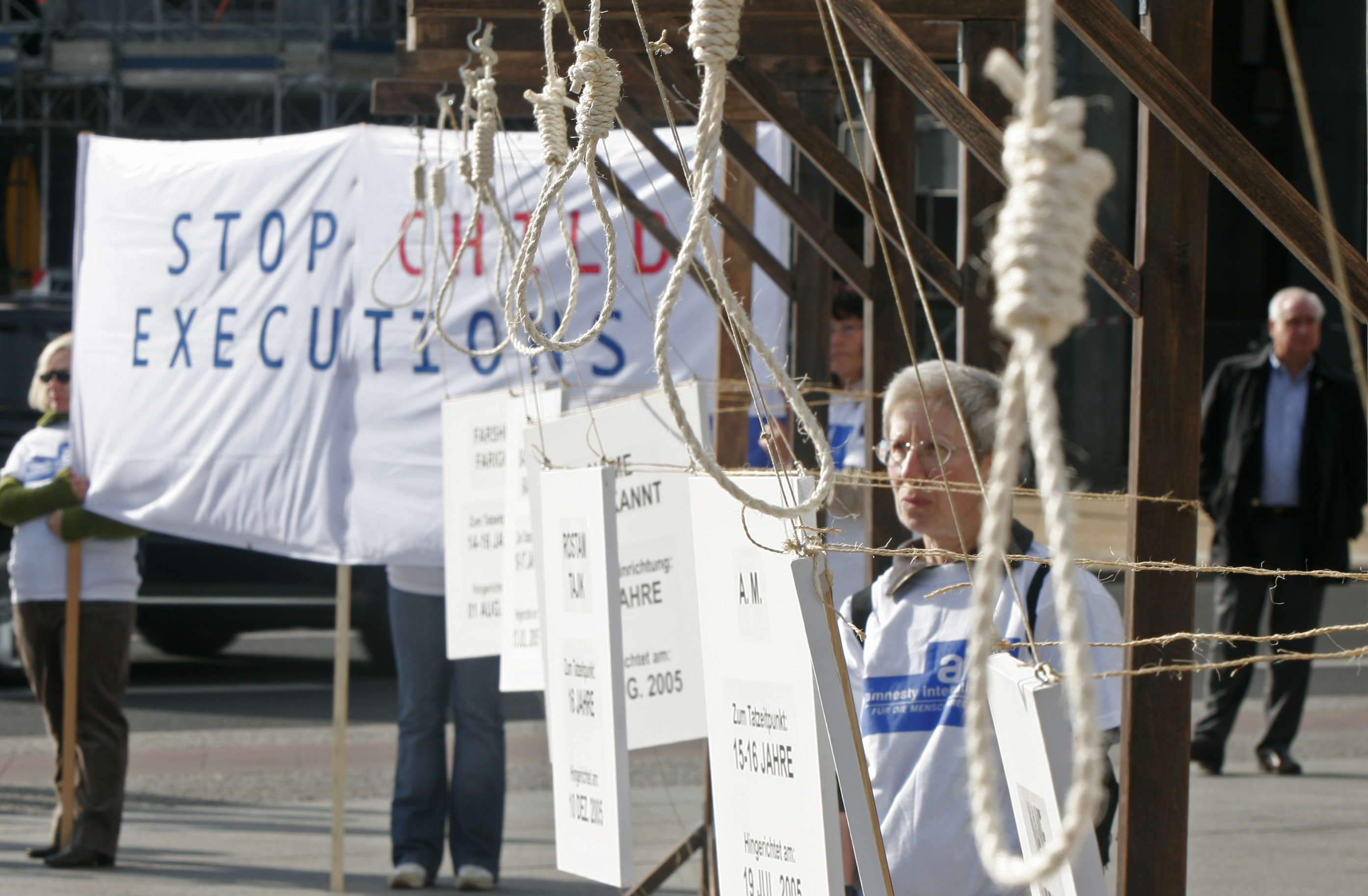 Mehrere Galgenstricke, im Hintergrund ein großes Banner mit der Aufschrift "Stop Child Executions"