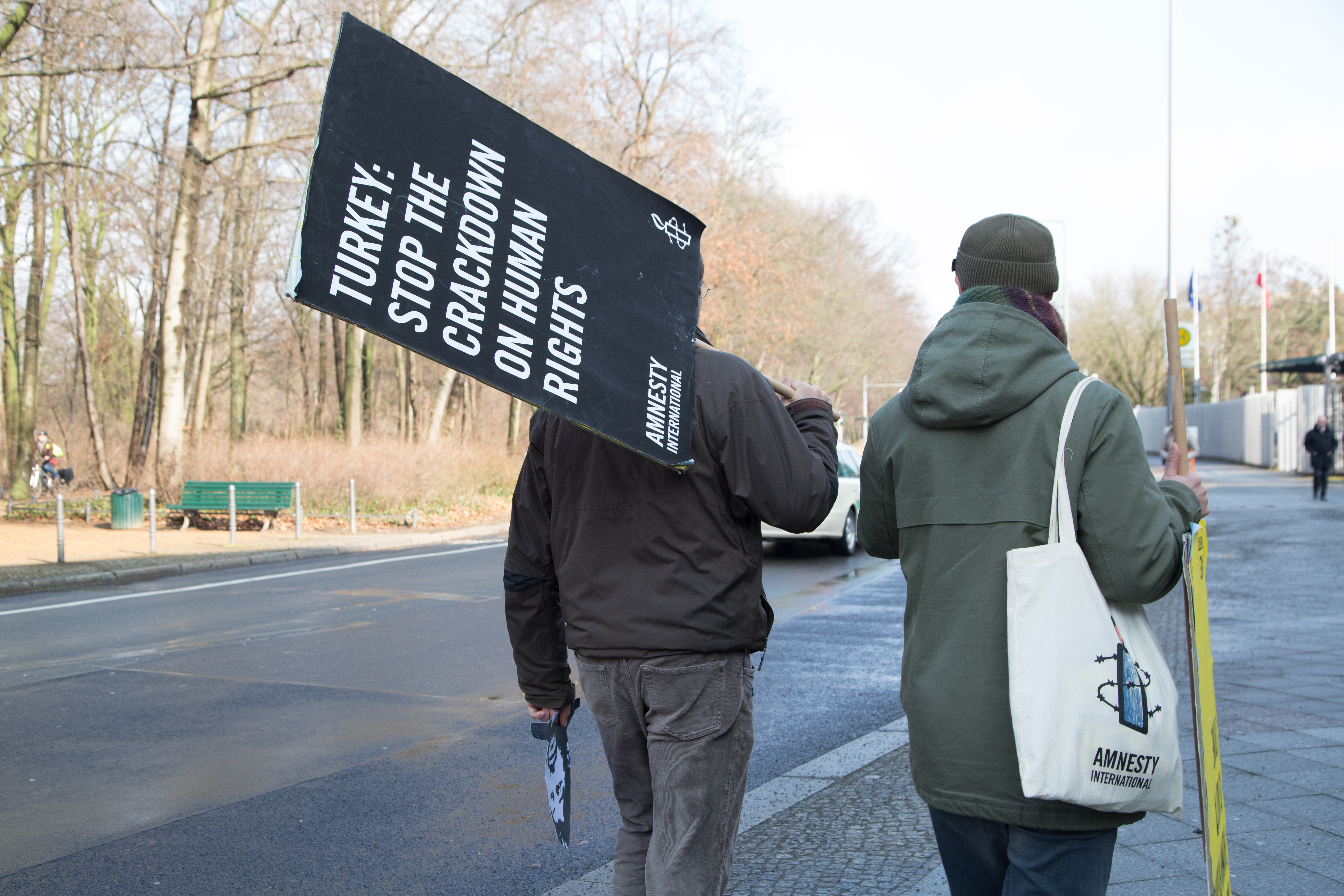 Zwei Männer laufen eine Straße entlang und tragen Amnesty-Protestschilder
