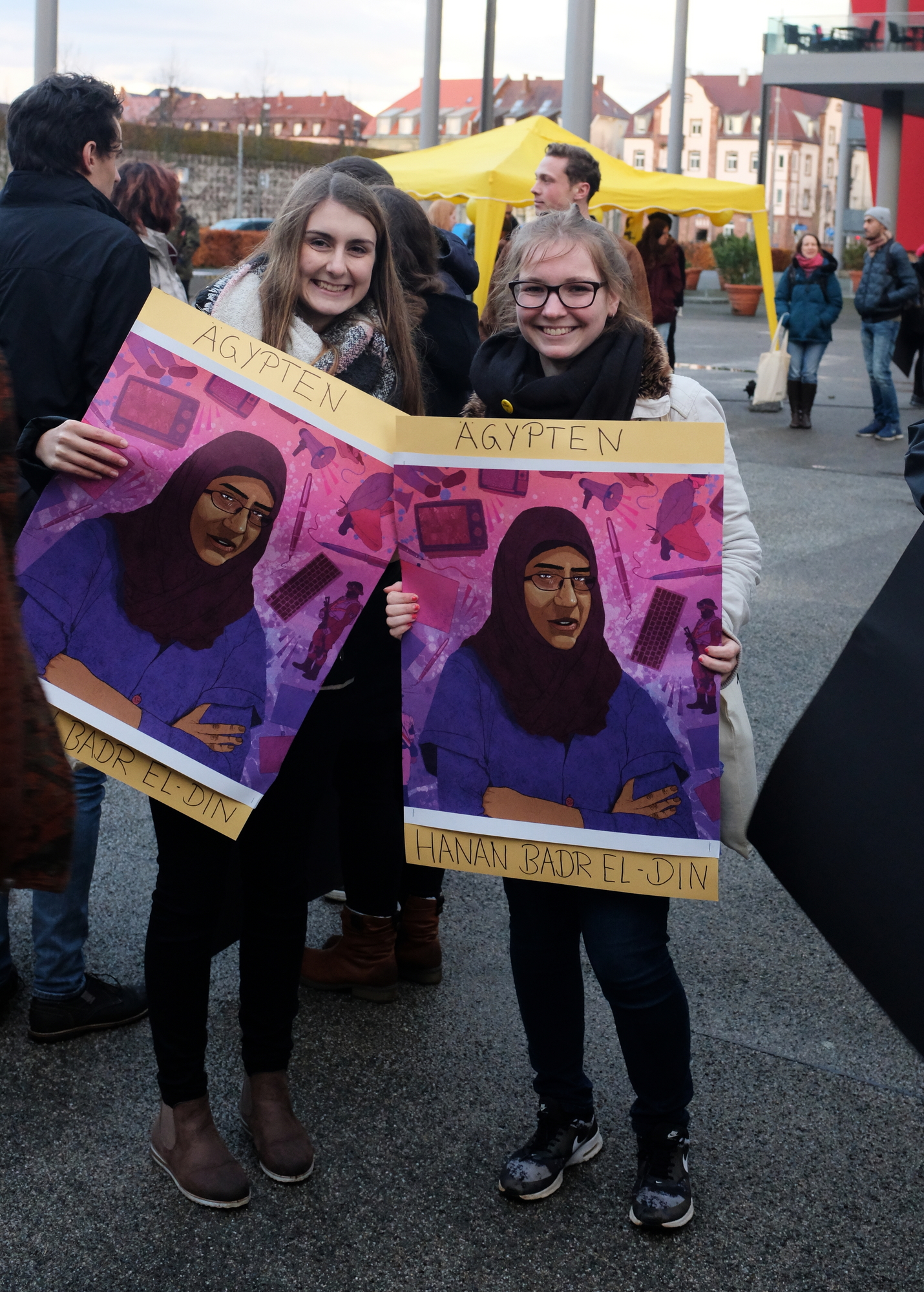 Zwei junge Frauen halten Plakate mit einer Grafik von Hanan Badr el-Din in der Hand