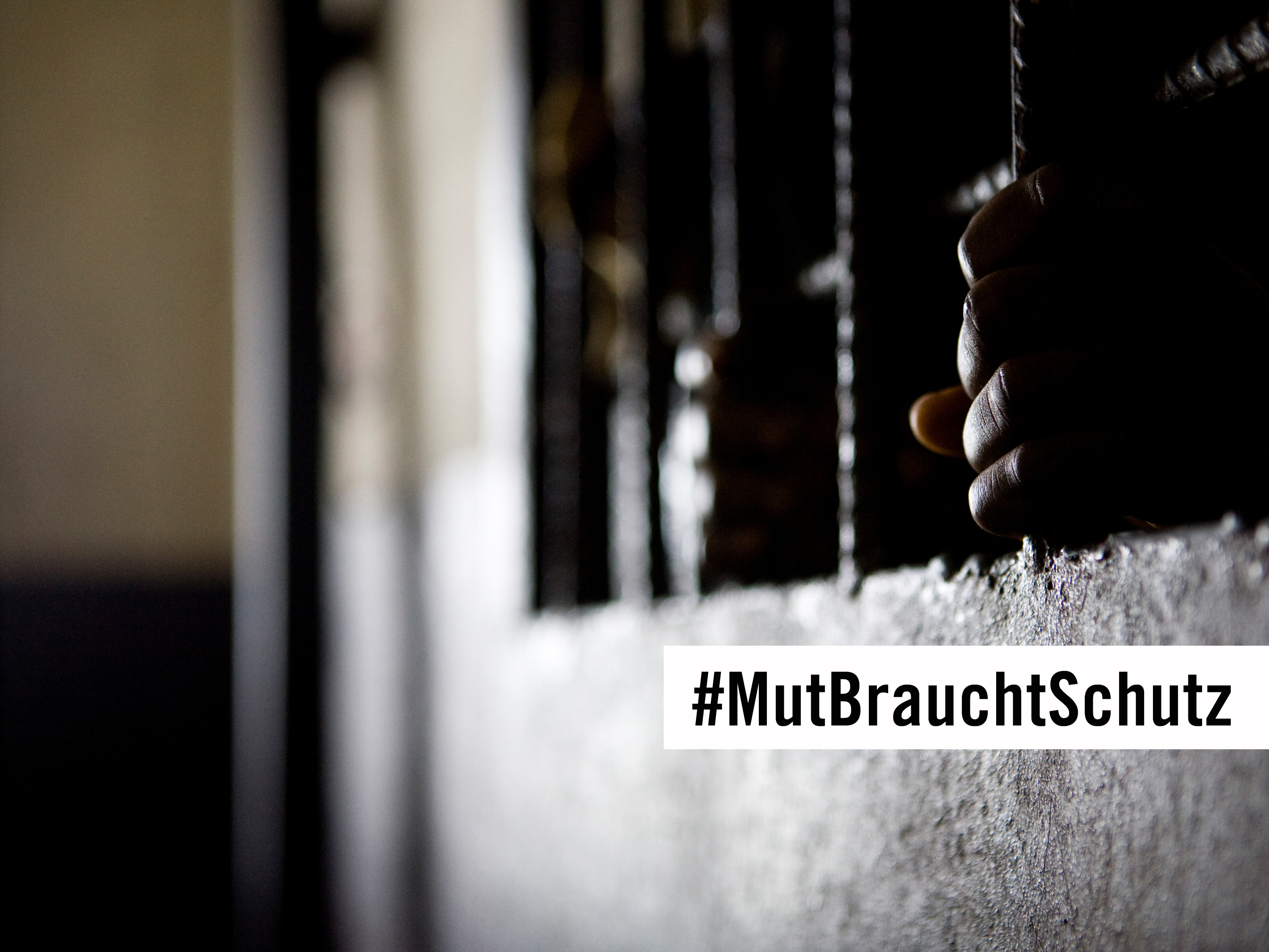 Undeutliches Foto zweier Hände, die Gitterstäbe umklammern; Schriftzug "#MutBrauchtSchutz"