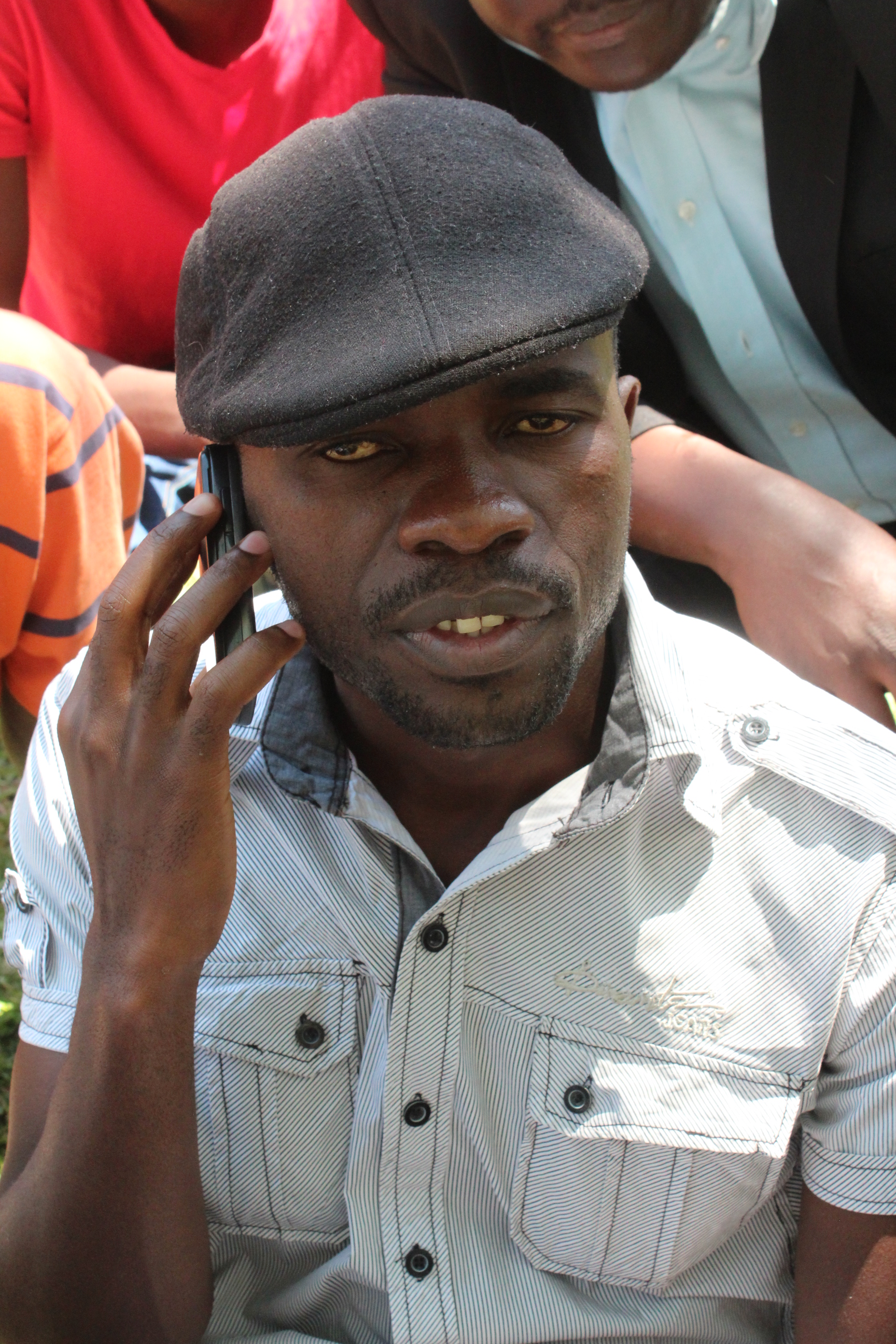 Das Foto zeigt Itai Peace Dzamara. Er trägt eine Mütze und hält ein Handy an sein rechtes Ohr. Hinter ihm stehen mehrere Personen.