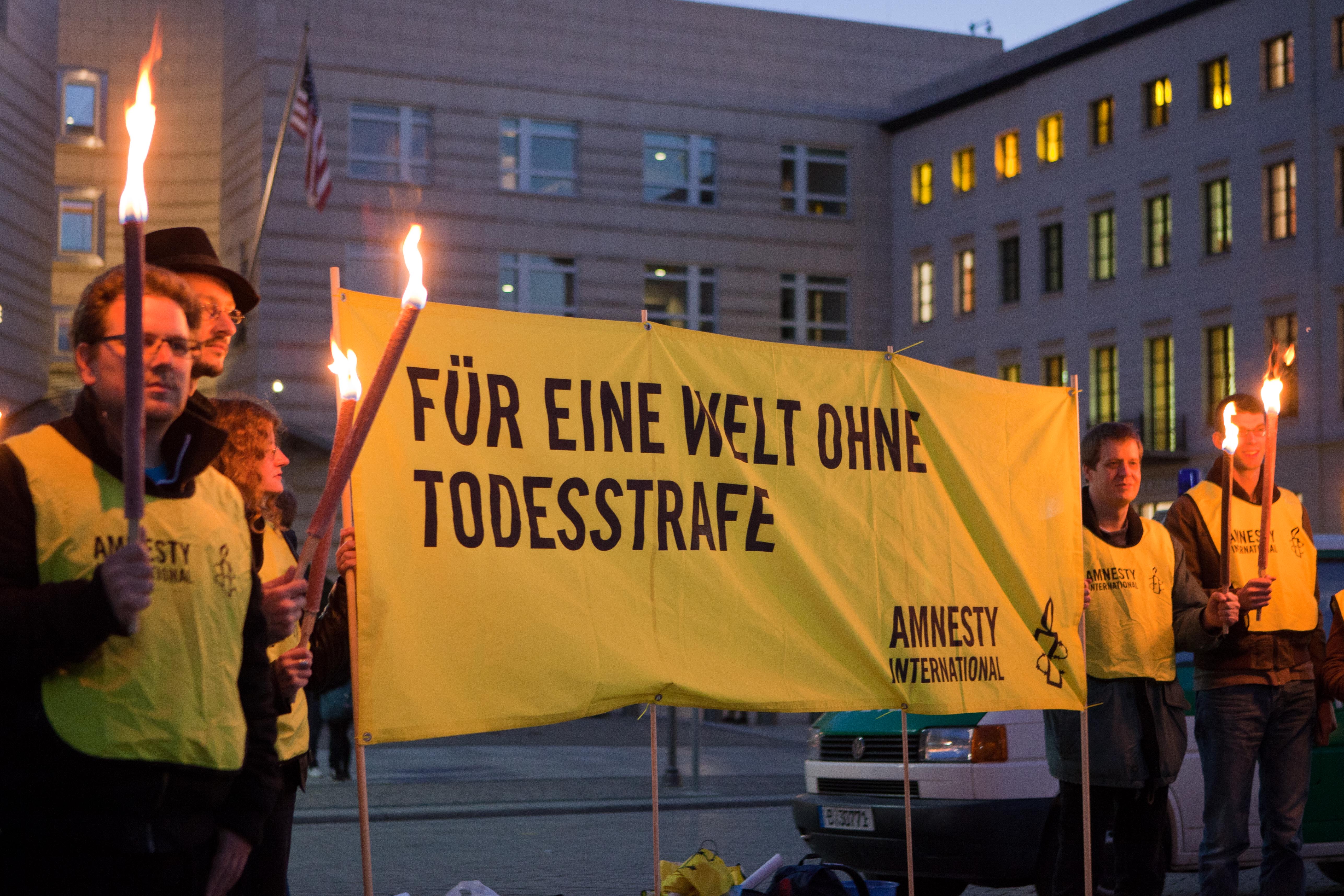 Mehrere Personen, die Fackel in den Händen halten, stehen neben einem Banner, auf dem steht: "Für eine Welt ohne Todesstrafe".