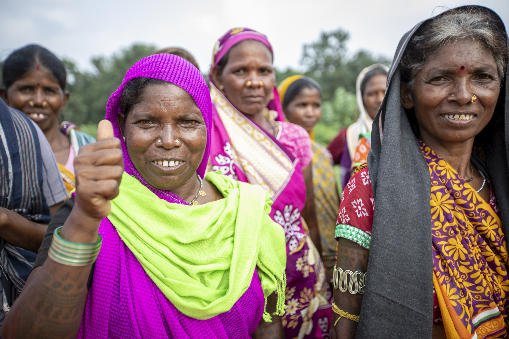 Pavitri Manjhi in einer Gruppe von Frauen. Sie lacht in die Kamera und zeigt "Daumen hoch".