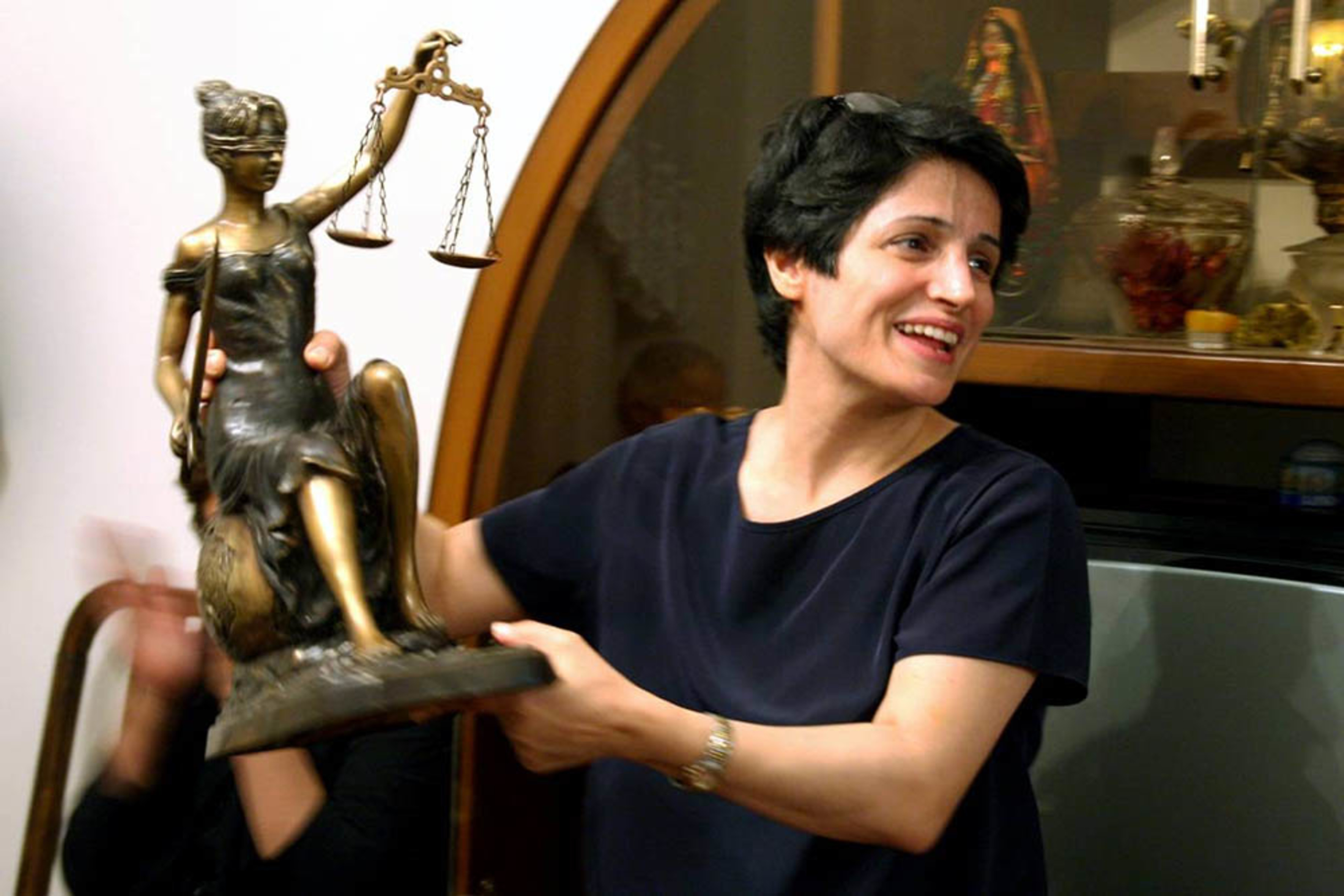 Foto einer lächelnden Frau, die nach rechts schaut und die eine Justitia-Skulptur in den Händen hält
