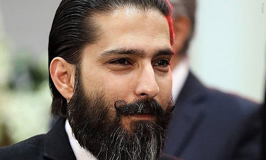 Ein Mann mit schwarzen Haaren und Anzug schaut freundlich an der Kamera vorbei