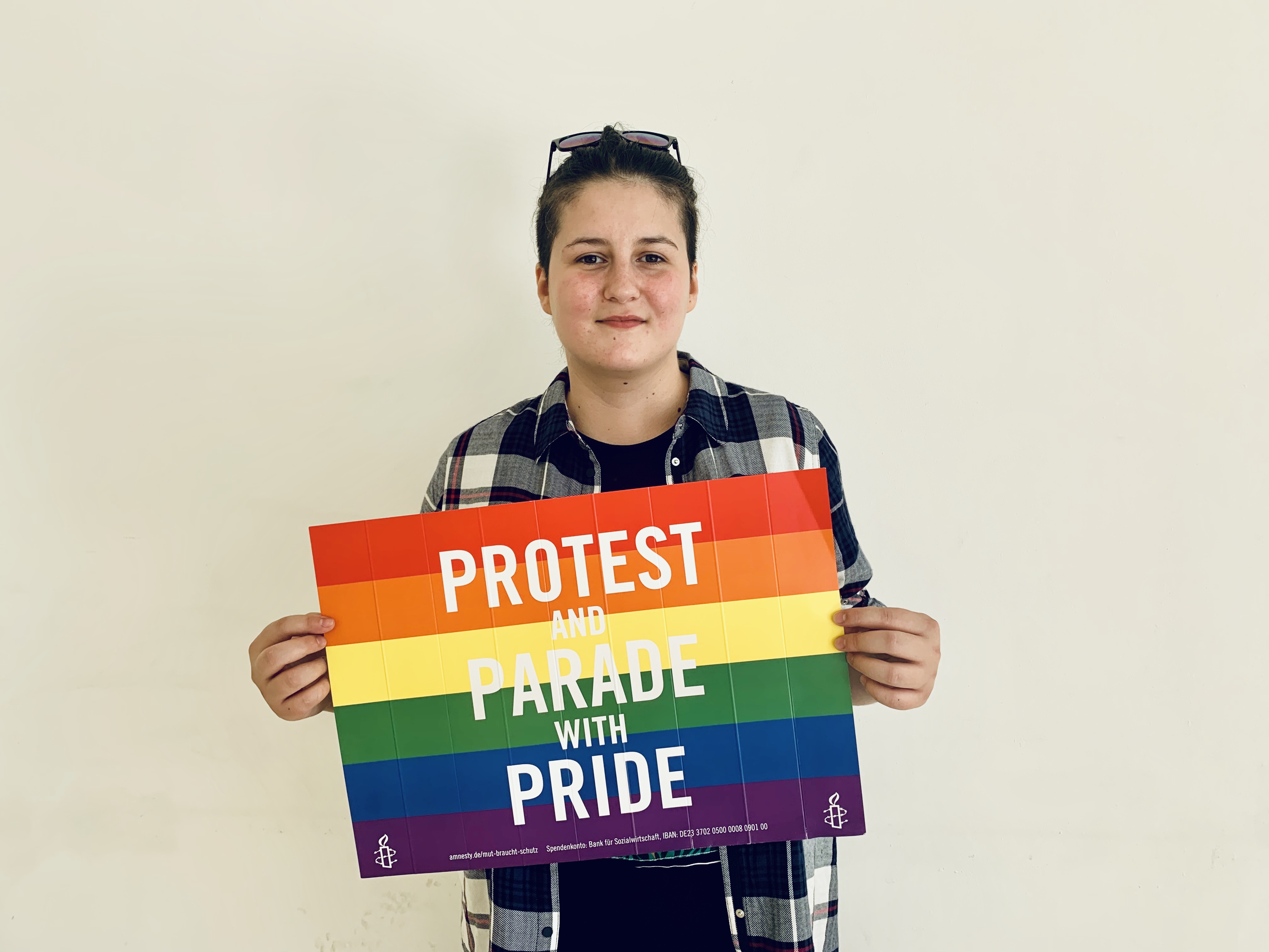 Vitalina Koval schaut frontal in die Kamera und hält ein Schild in Regenbogenfarben vor sich. Auf dem Schild steht "Protest and Parada with Pride" geschrieben.