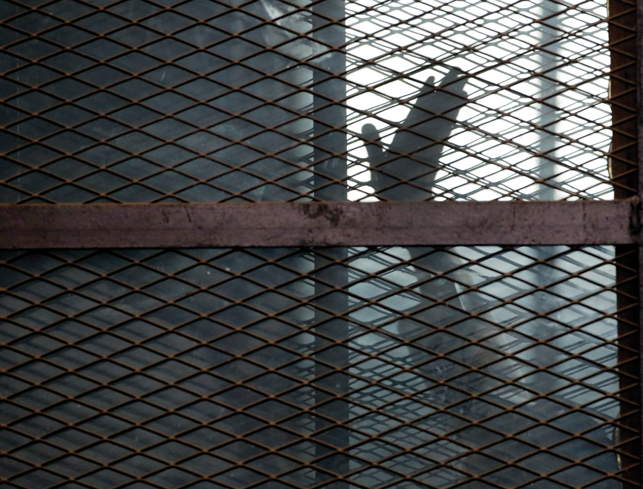 Eine Person hinter komplett vergitterten Scheiben hebt den Arm