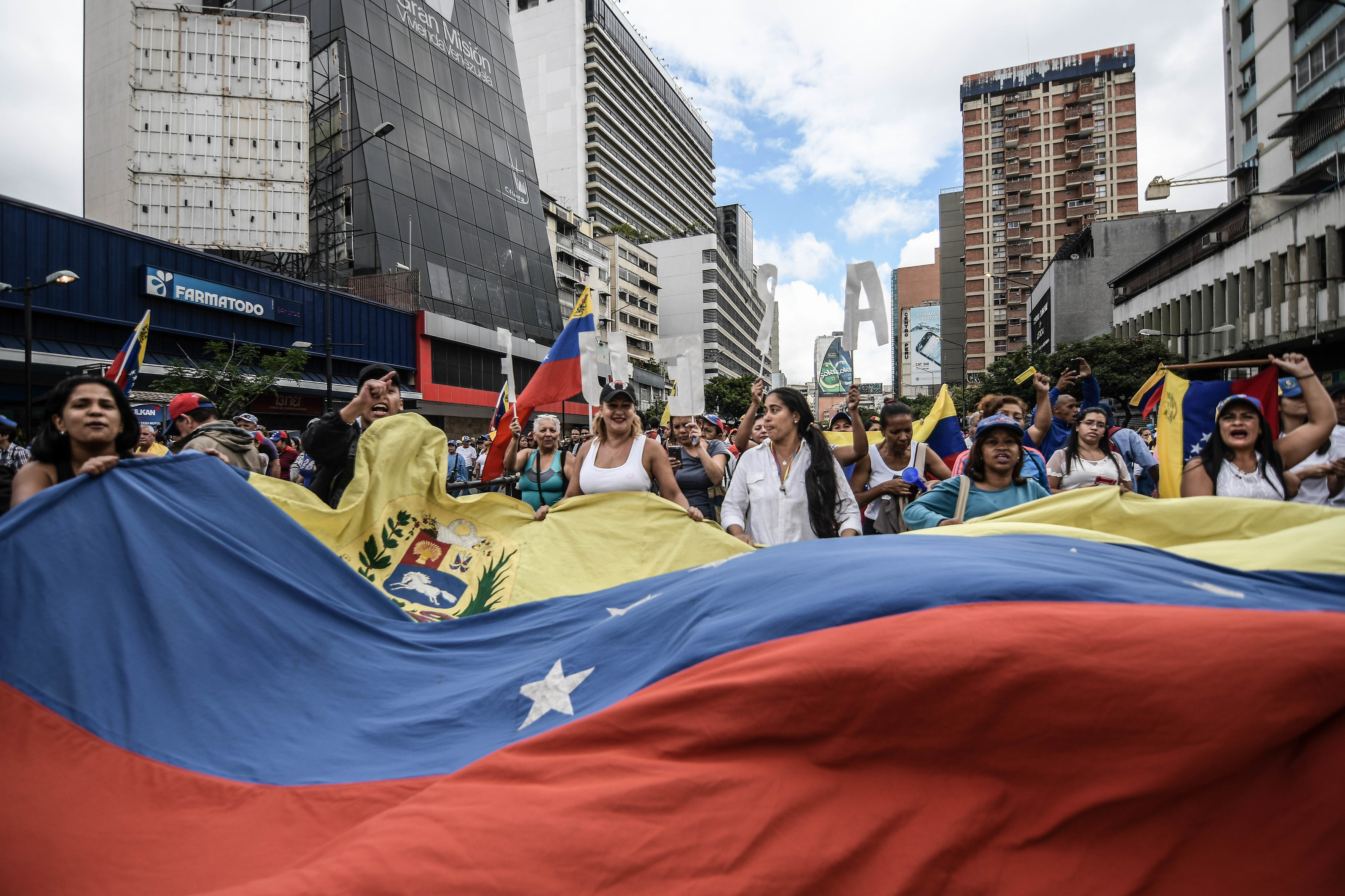 Eine große Menschenmenge zieht durch die Straße und breitet eine sehr große venezolanische Flagge aus