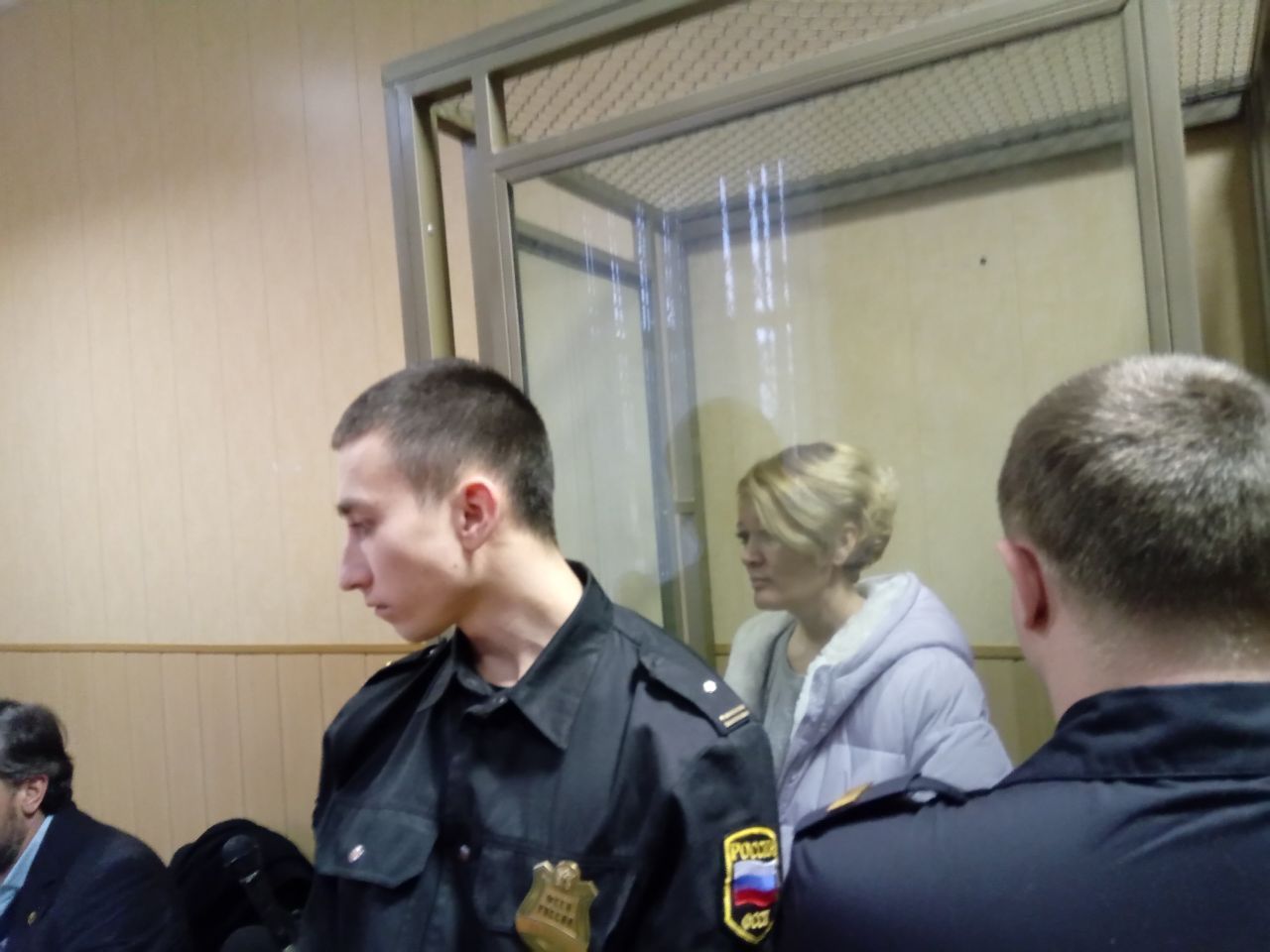 Anastasia Shevchenko im Hintergrund bei der Verhandlung in einem Glaskasten zu sehen.