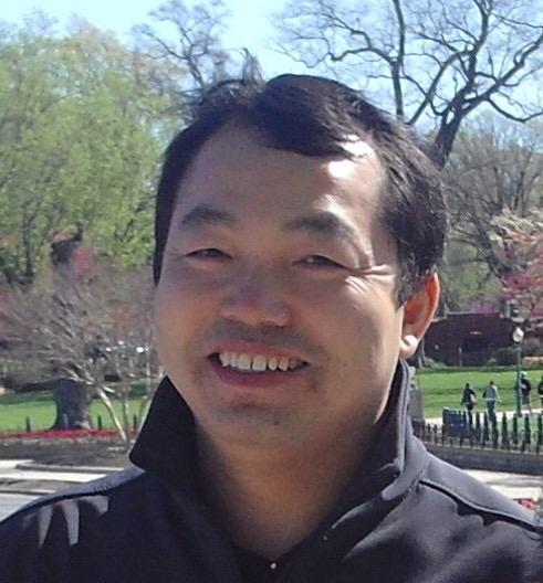 Portraitfoto eines Mannes mittleren Alters, der in einem Park steht und in die Kamera lächelt.
