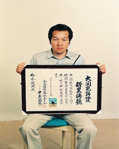 Porträtfoto von Matsumoto Kenji mit einer Zeichnung auf seinem Schoß