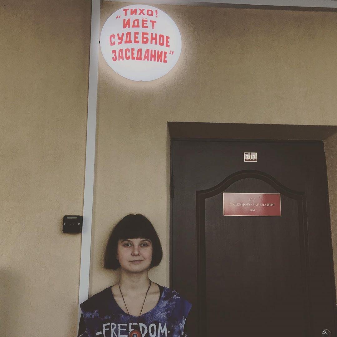 Eine junge Frau steht neben einer dunklen Holztür an einer Wand. 