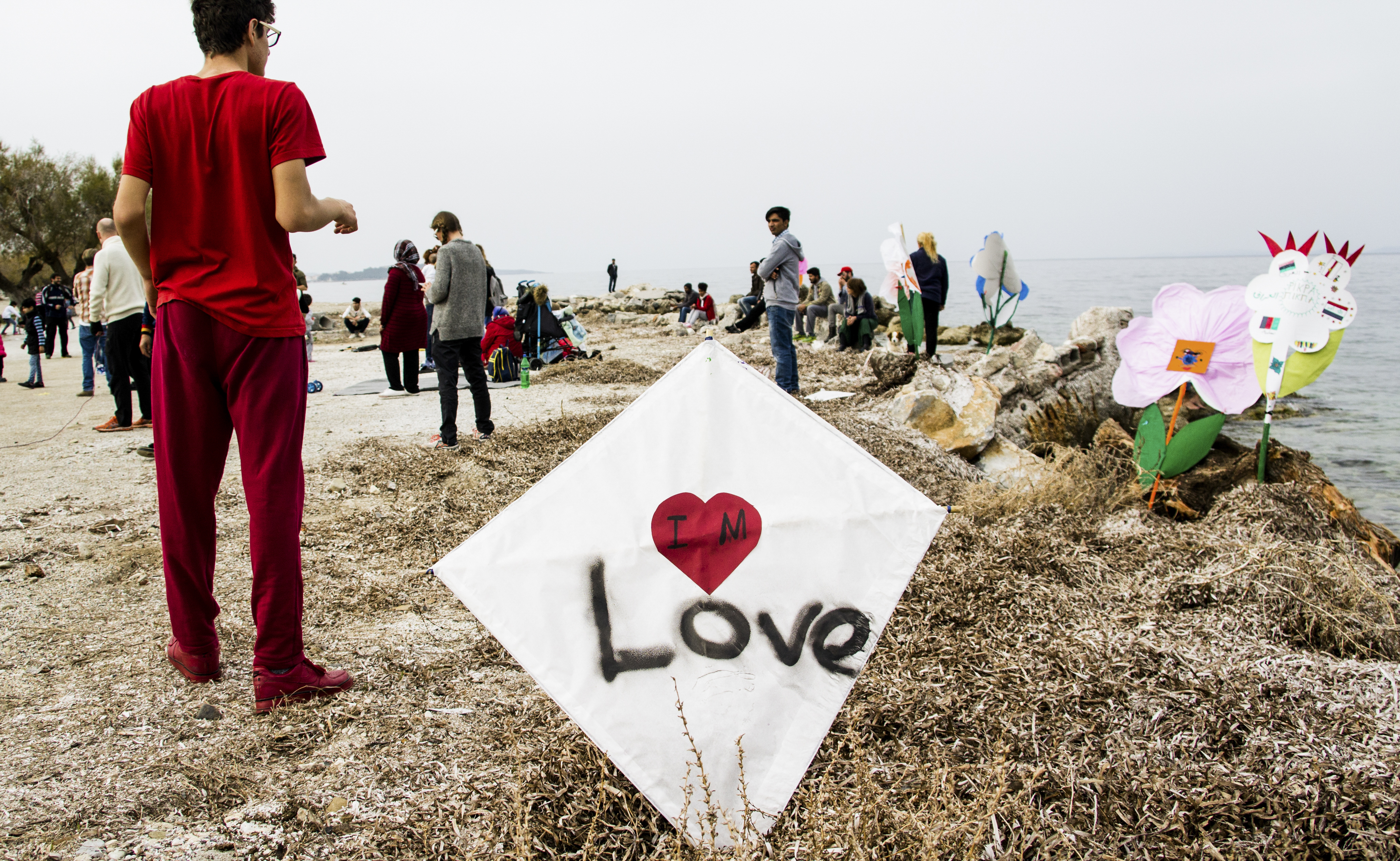 Im Vordergrund befindet sich ein Drachen mit Herz und der Aufschrift "Love", daneben steht ein Junge. Im Hintergrund sind weitere Menschen zu sehen.