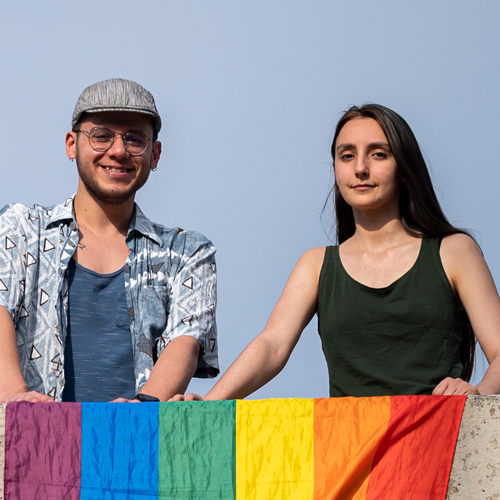 Özgür Gür und Melike Balkan mit einer Regenbogenfahne auf einer Mauer vor ihnen