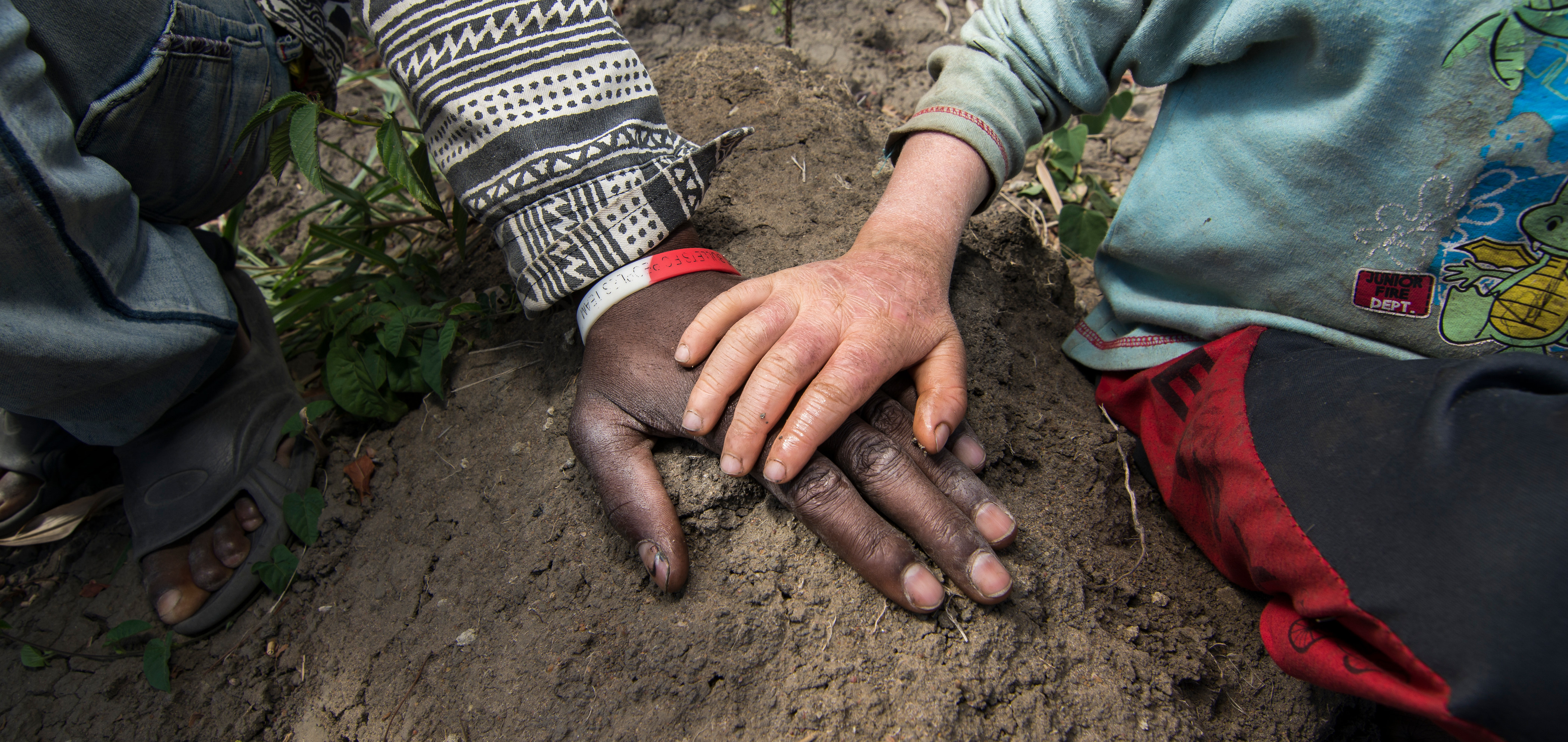 Eine Kinderhand mit heller Haut auf einer großen Hand mit dunkler Haut.