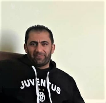 Porträt eines Mannes, der einen dunklen Kapuzenpullover trägt und die Kamera lächelt.