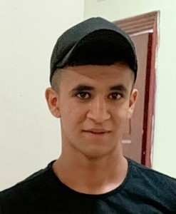 Ein junger Erwachsener mit schwarzer Kappe und schwarzem T-shirt guckt in die Kamera