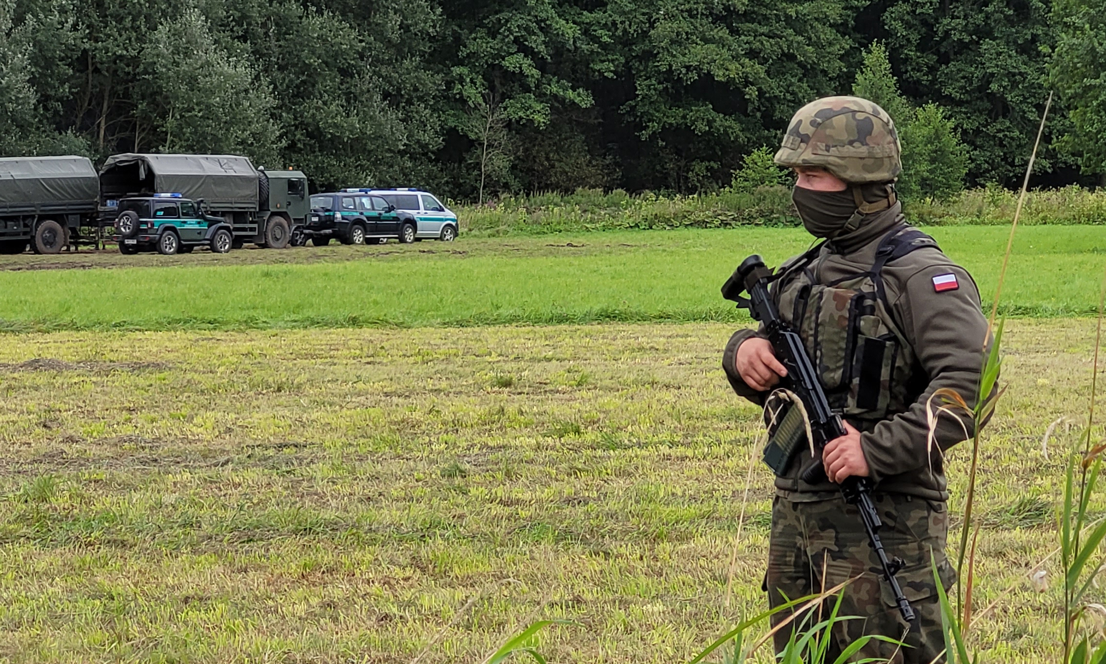 Das Bild zeigt einen Soldat mit schwerer Bewaffnung, er steht auf einem Feld, im Hintergrund ein Waldstück