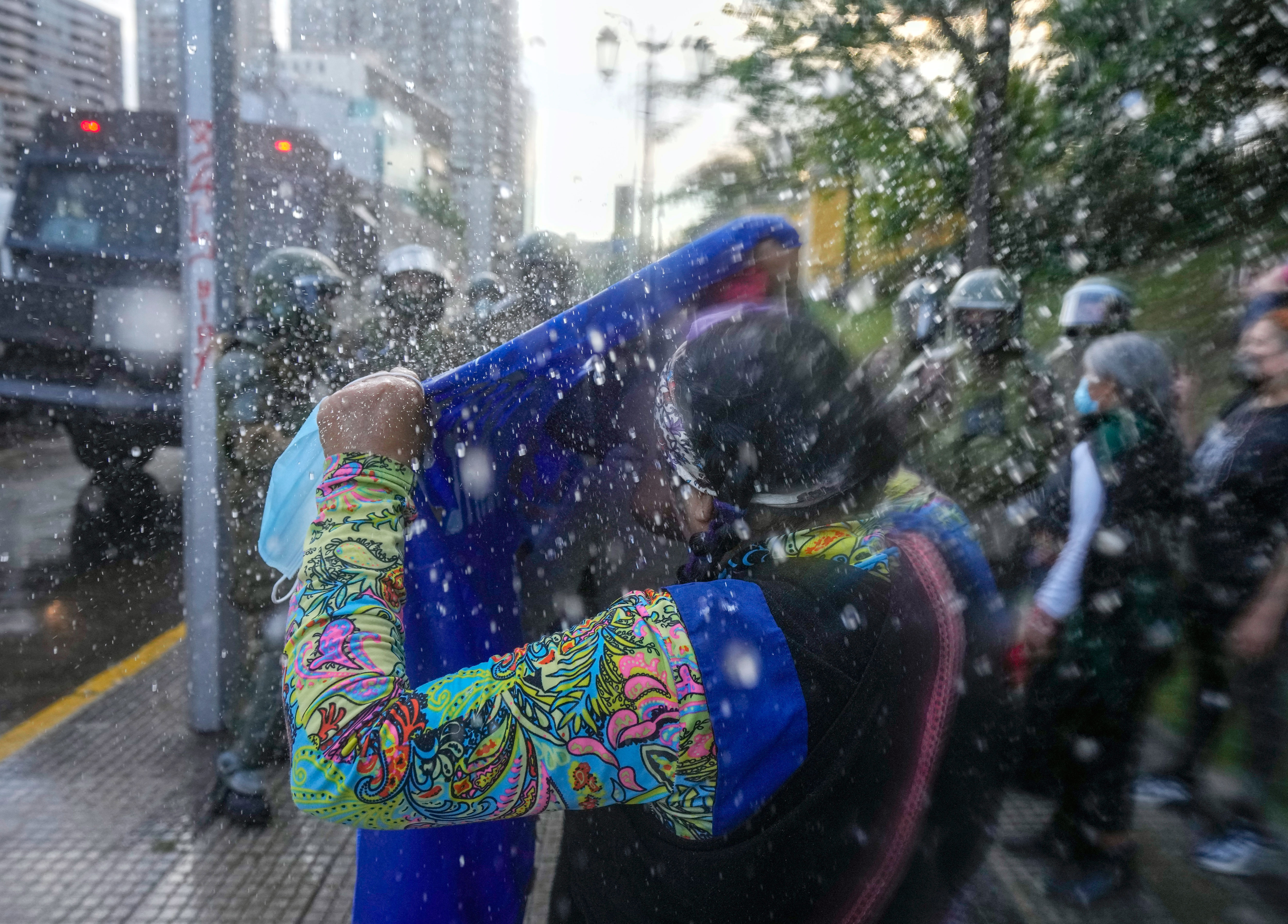 Eine Frau steht vor einer Gruppe von Polizisten mit Helmen und hält ein Tuch in die Höhe, um sich vor spritzendem Wasser zu schützen.