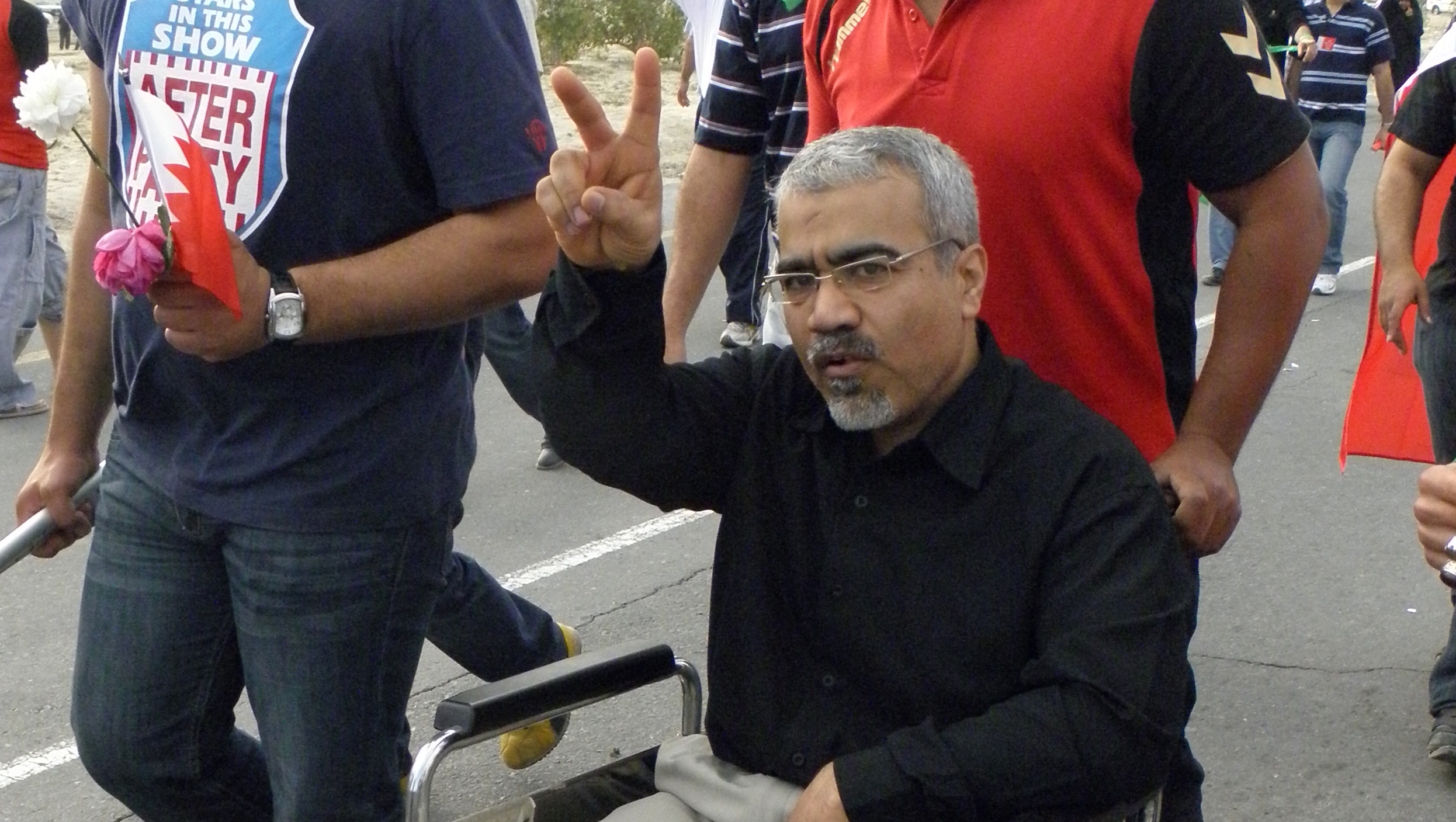 Das Bild zeigt einen Mann der in einem Rollstuhl sitzt und die Hand zum Victory-Zeichen hebt.