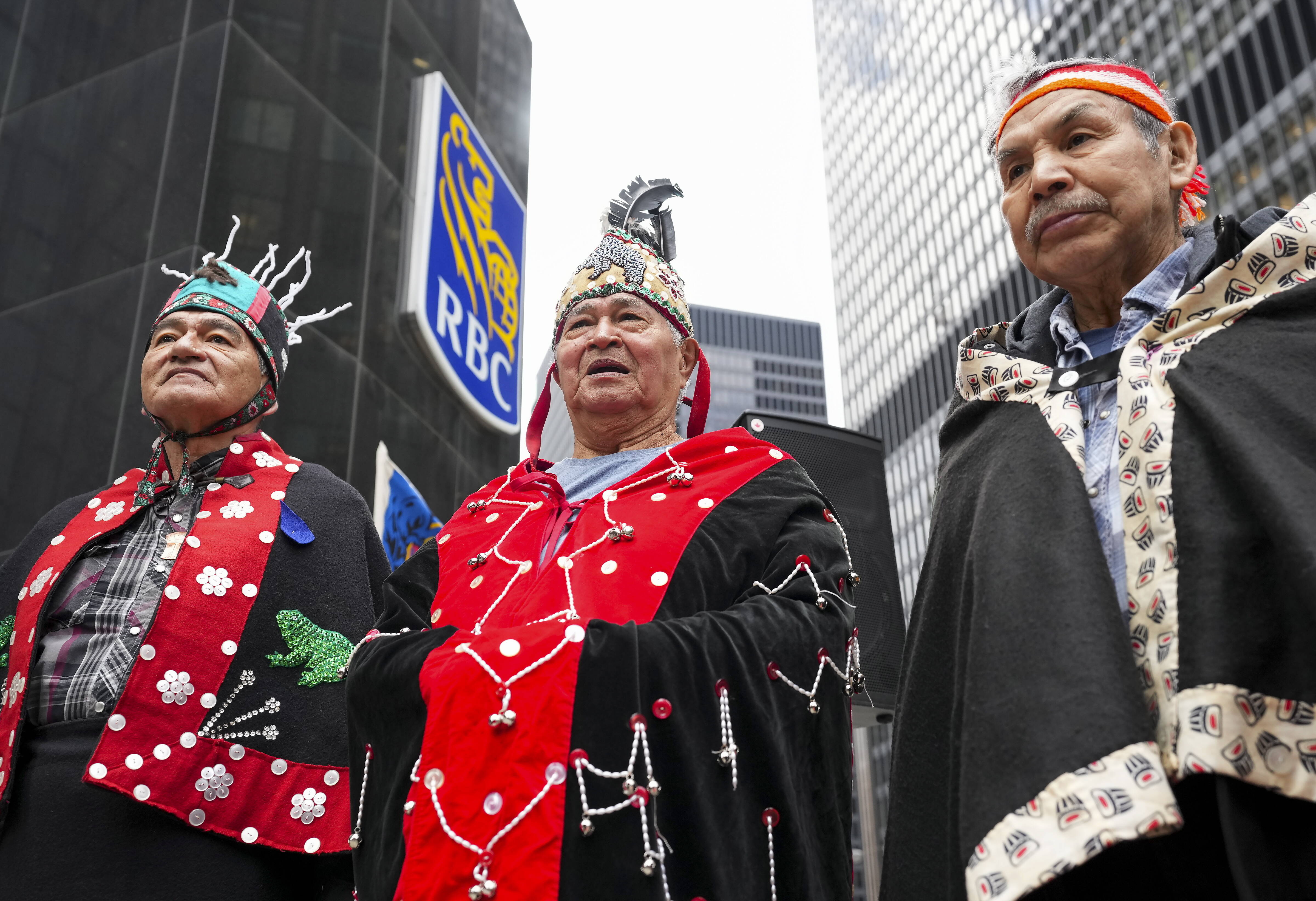 Drei Männer in traditioneller Bekleidung stehen vor einem Gebäude und schauen in die Kamera