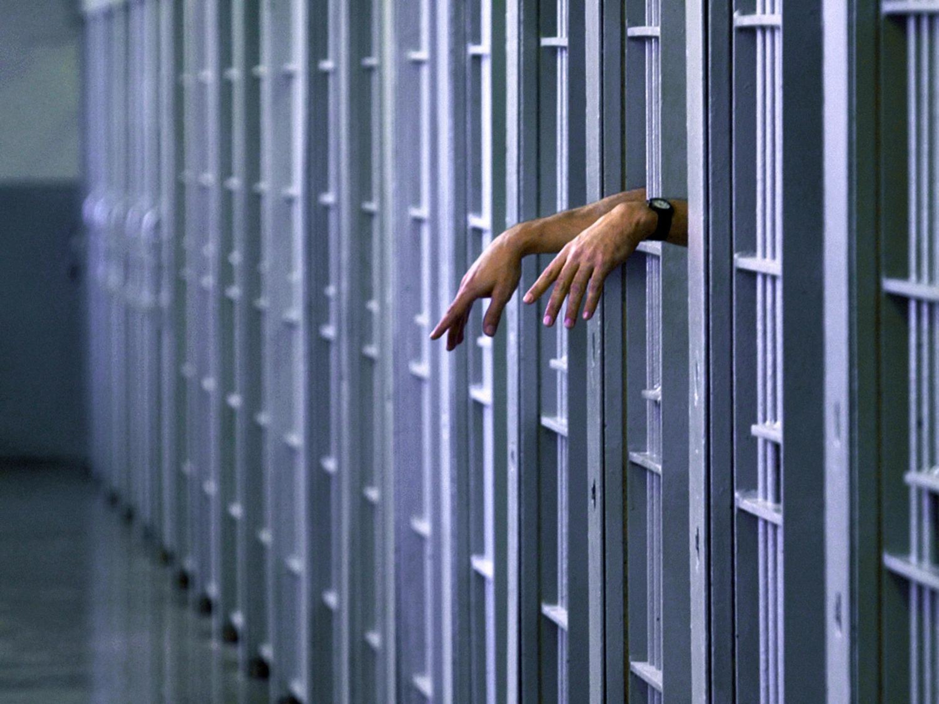 Eine Person hält ihre Hände aus den Gitterstäben ihrer Gefängniszelle.