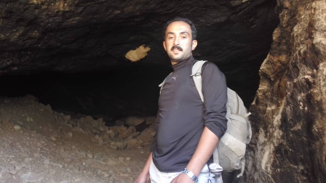 Das Bild zeigt einen Mann mit Rucksack, der vor einem Felsvorsprung steht