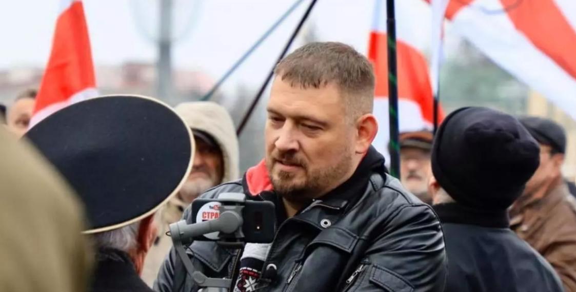 Das Bild zeigt einen Mann, der auf einer Demonstration in eine Kamera spricht