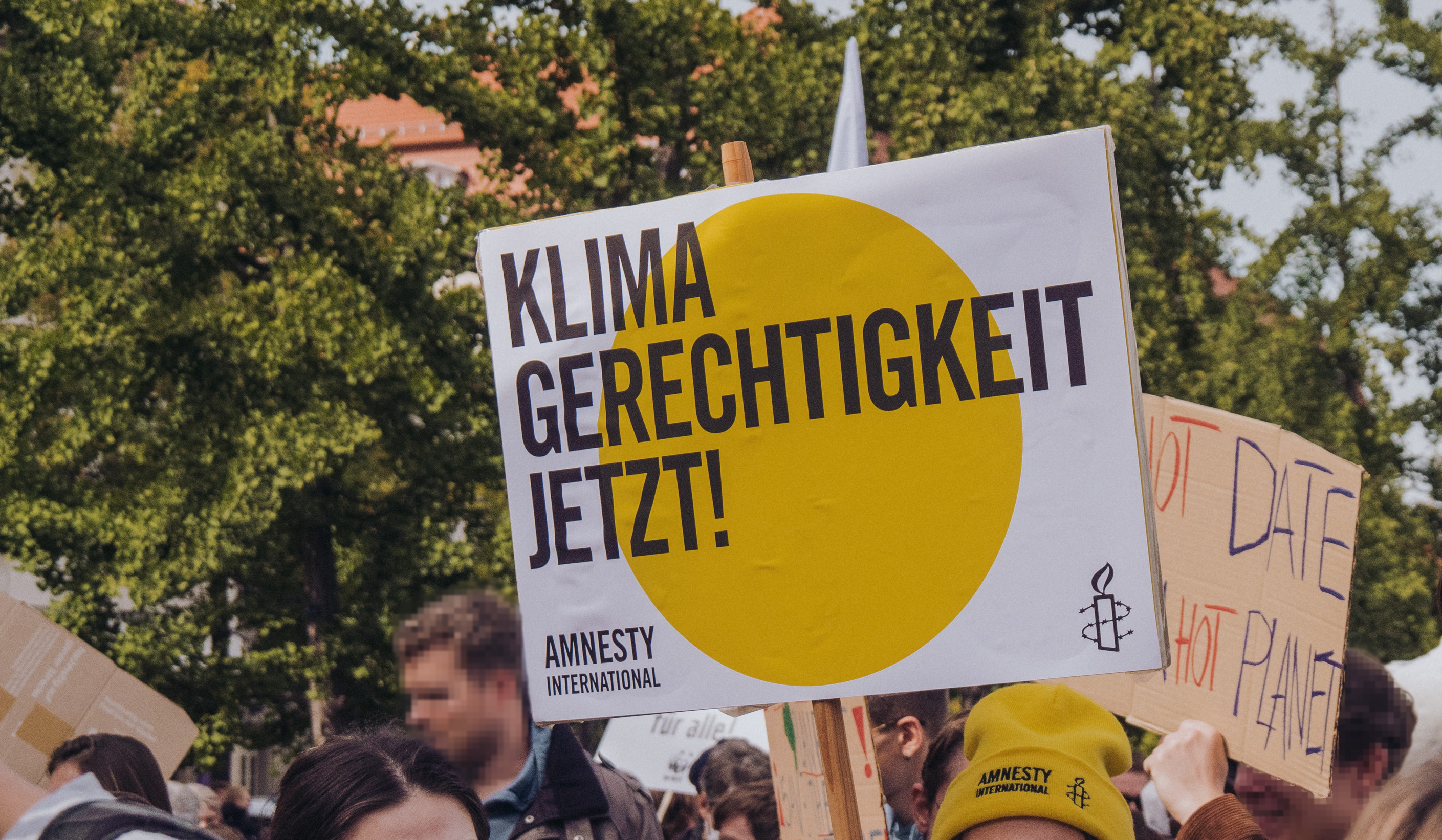 Das Foto zeigt eine dichtgedrängte Menschenmenge auf einer Demonstration. Eine junge Frau mit Amnesty-Mütze hält ein Schild mit Amnesty-Logo hoch. Auf dem Foto steht: "Klimagerechtigkeit jetzt!".