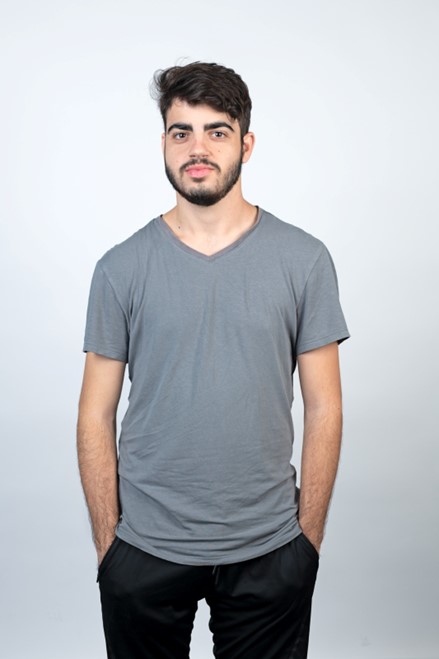 Das Foto zeigt einen jungen Mann, der vor einer Wand steht und der Jeans und T-Shirt trägt. Beide Hände hat er in den Hosentaschen.