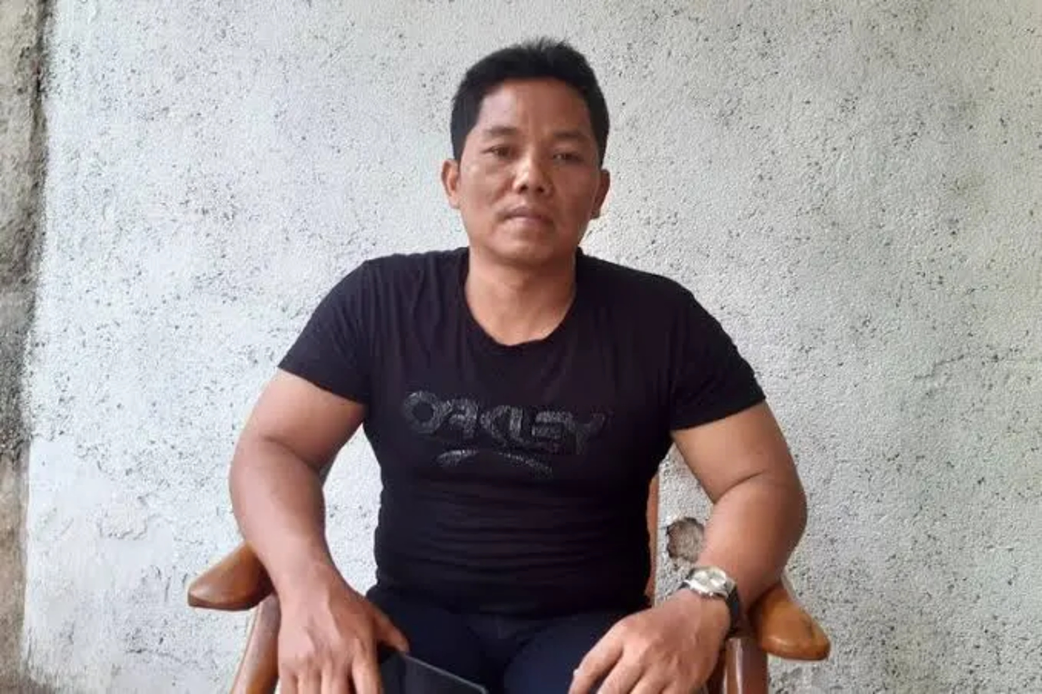 Heri Budiawan trägt ein T-Shirt und sitzt auf einem Stuhl mit beiden Armen auf den Lehnen und blickt ernst in die Kamera. 
