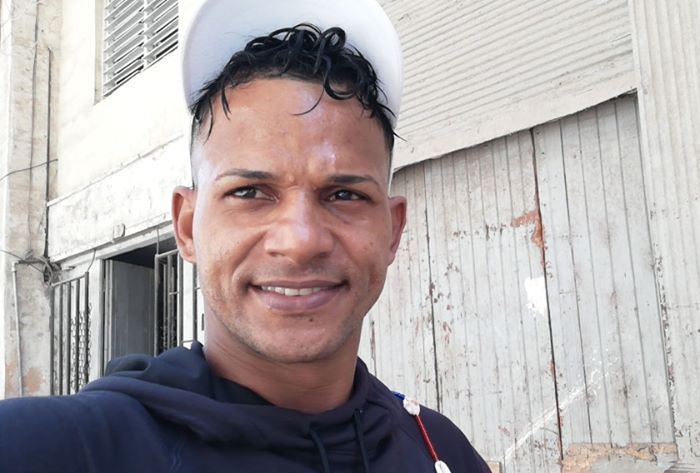 Ein junger Mann in einem dunklen Kapuzenpulli mit einer weißen Kappe lacht in die Kamera, als er ein Selfie aufnimmt. Es sit der als "Maykel Osorbo" bekannte kubanische Musiker Maykel Castillo Pérez