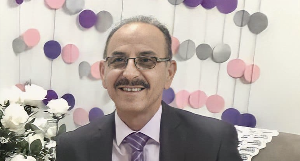 Porträtgoto von Bassem al-Zaak mit Brille und Schnäuzer. Er trägt einen Anzug und eine Krawatte und lächelt in die Kamera.
