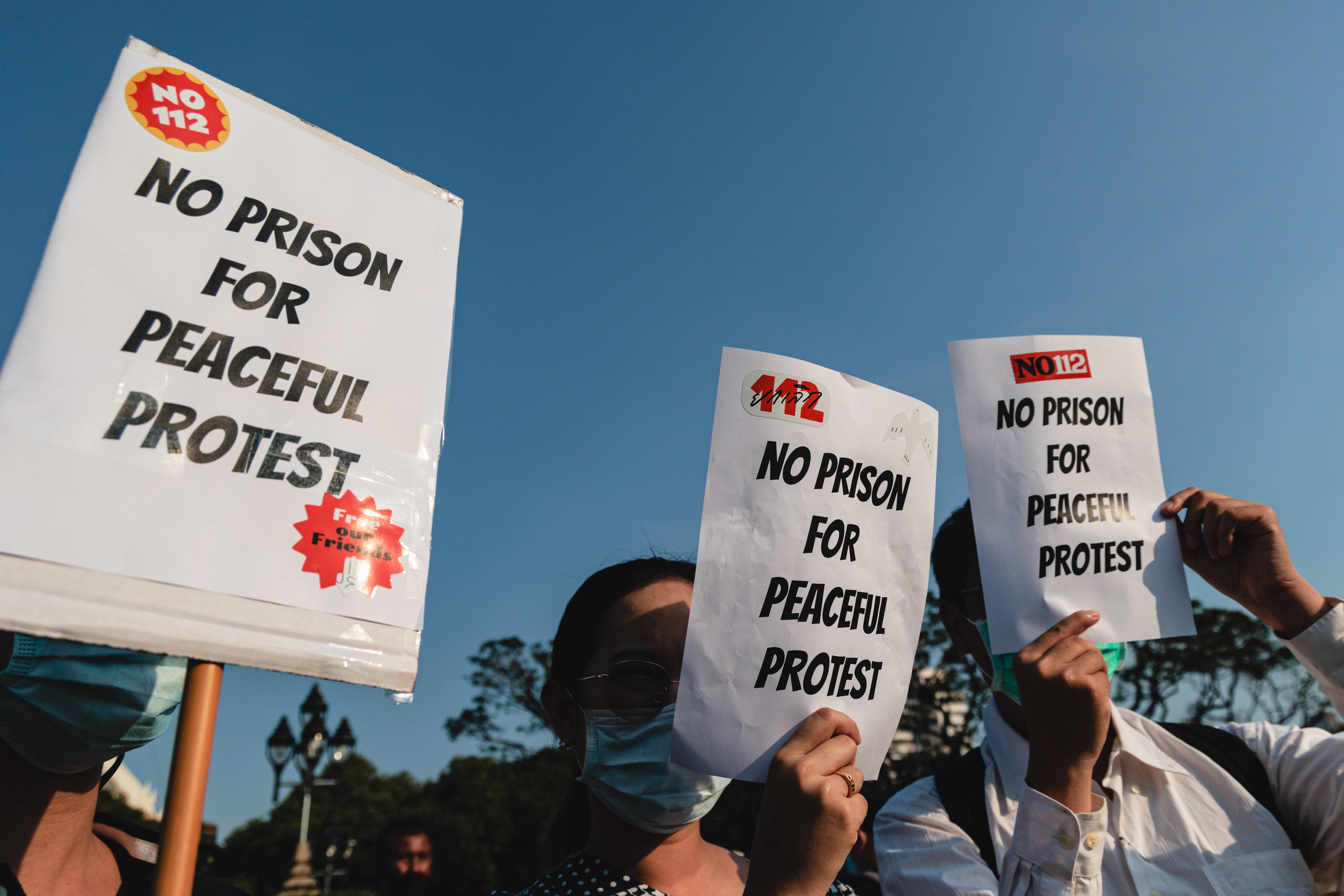 Das Foto zeigt drei Personen bei einer Demonstration. Sie halten Schilder hoch, auf denen steht: "No prison for peaceful protest".