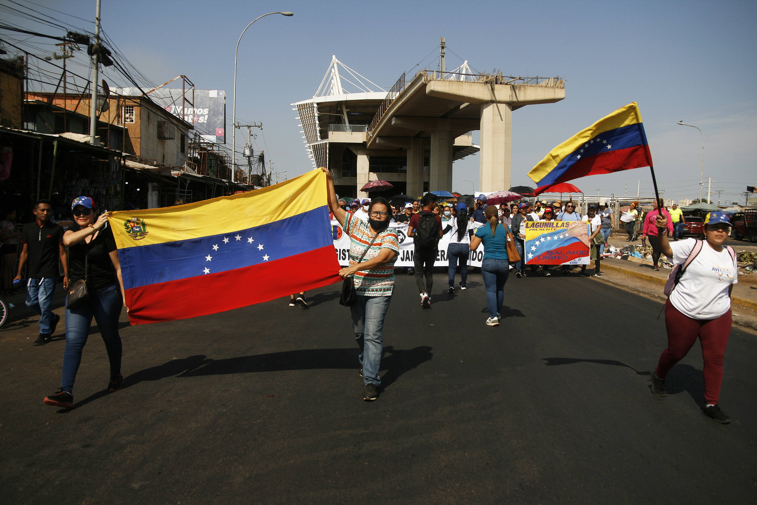 Das Bild zeigt viele Menschen auf einer breiten Straße, manchen halten die Nationalflagge Venezuelas in der Hand